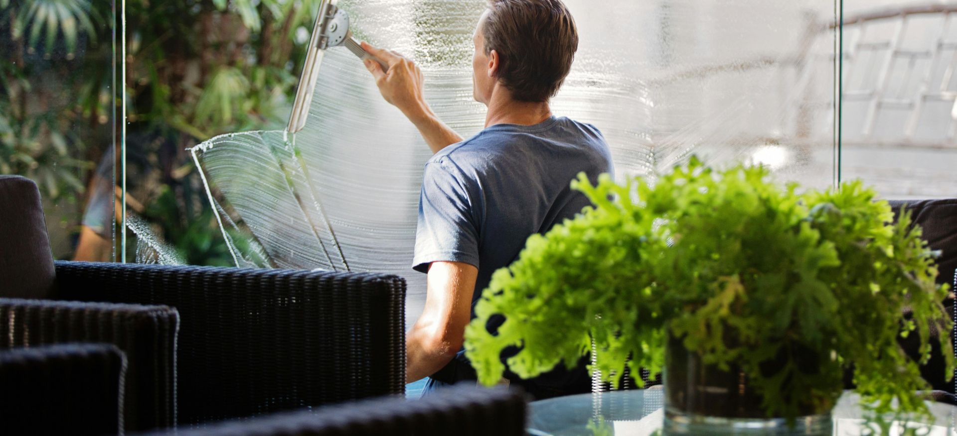 Man in Gray Shirt Cleaning Clear Glass Wall Near Sofa