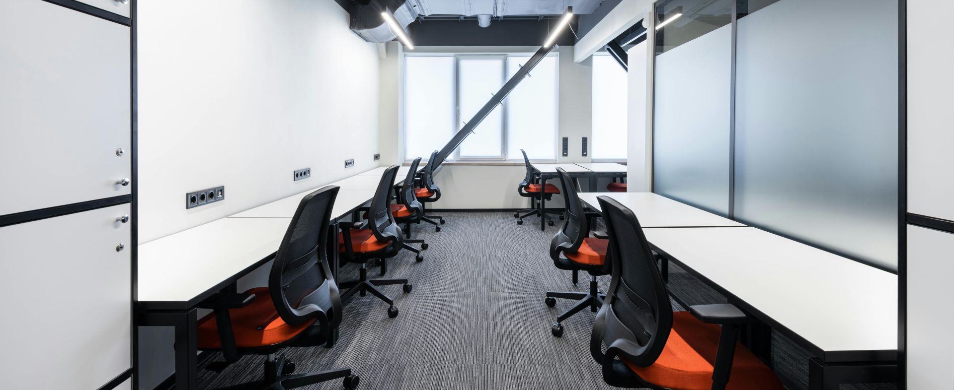 White desks with comfortable colorful chairs placed in spacious workspace with window and glass partitions in contemporary financial business center