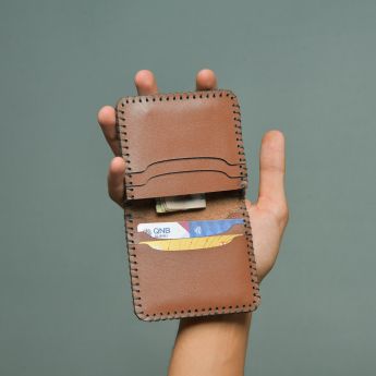A hand holding a leather wallet containing various cards and cash.